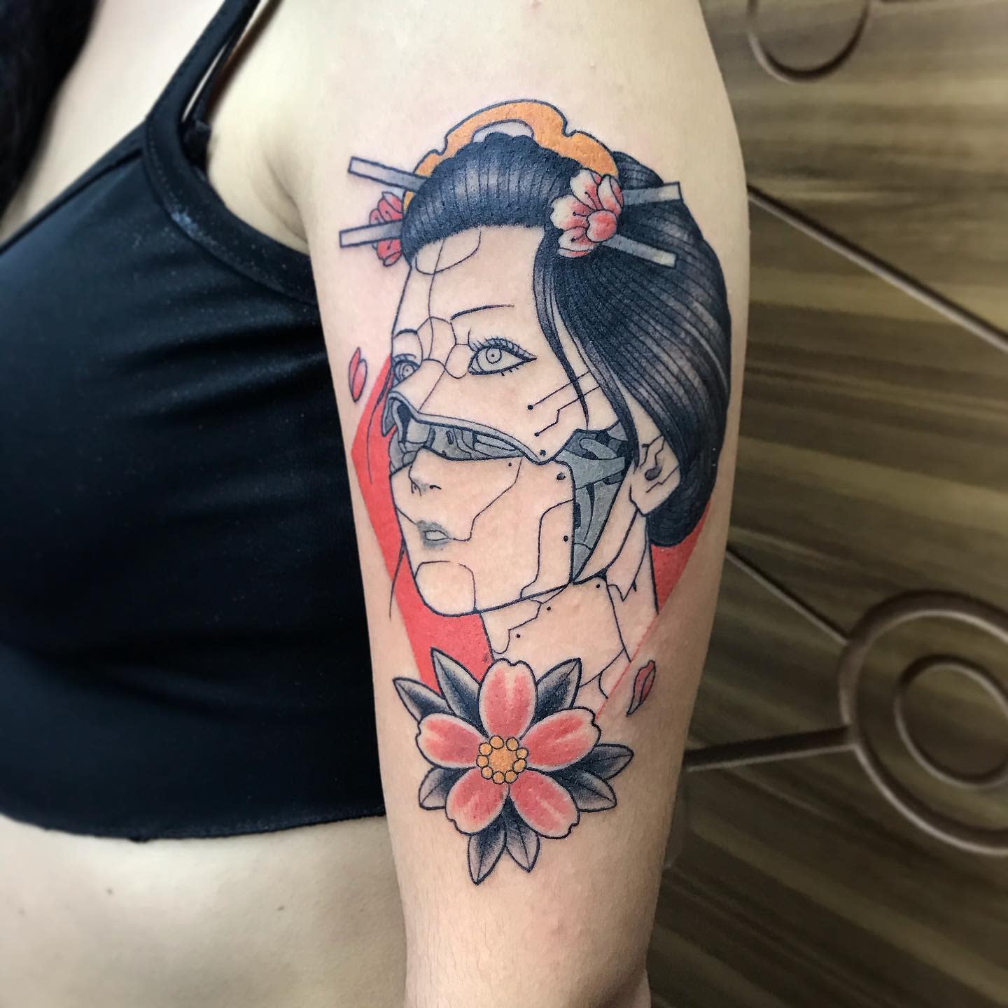 Cyberpunk tattoo on upper arm depicting a female cyborg with a geisha-inspired design and a flower below